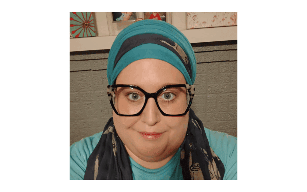 Christian woman wearing teal and navy headwrap and black cateye glasses.