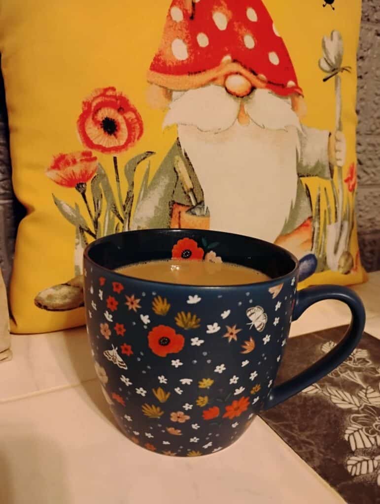 A cup of coffee in a navy mug with orange, yellow, and white flowers on it.
