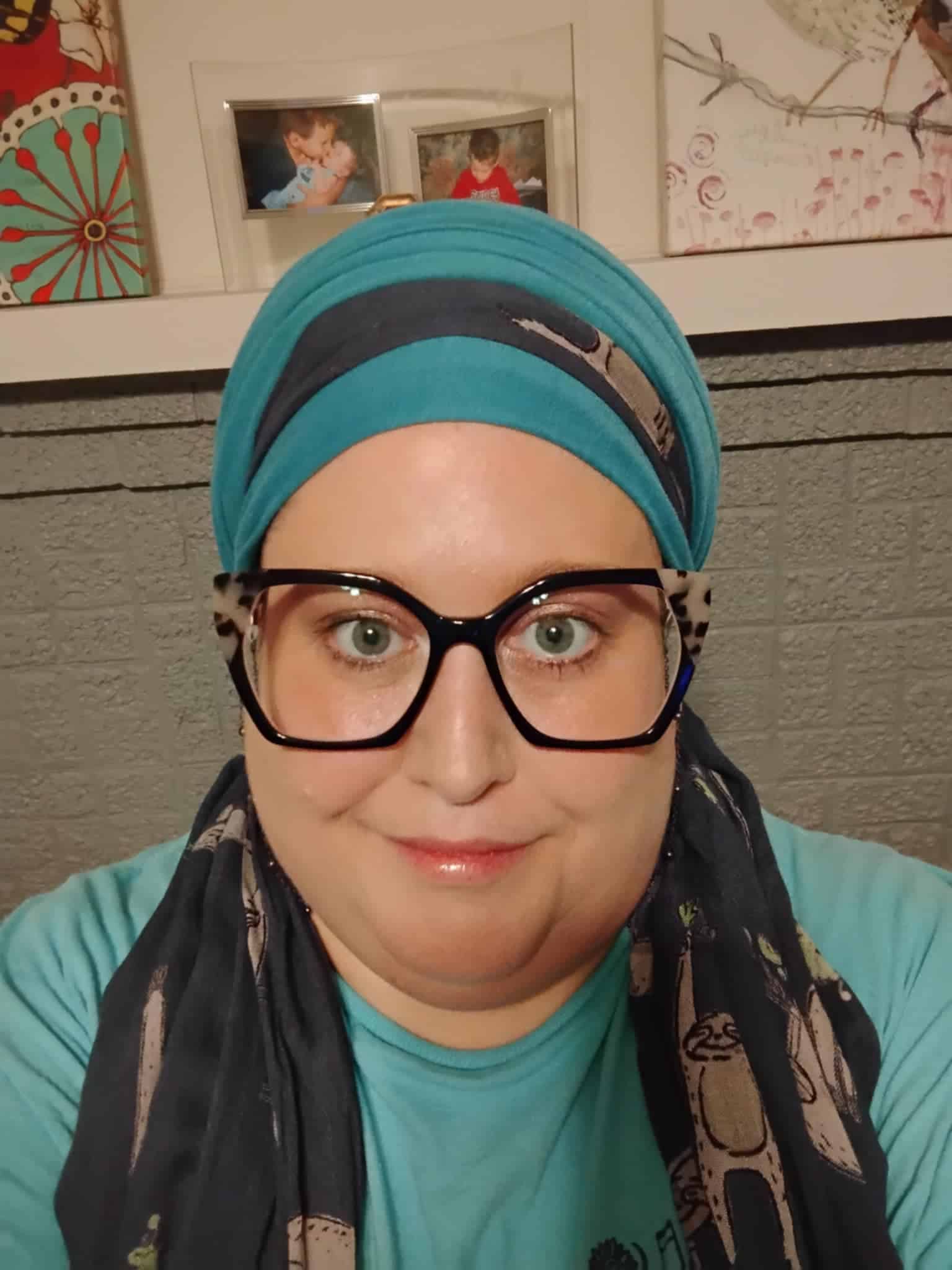 Christian woman wearing teal and navy headscarves and black cateye glasses. 