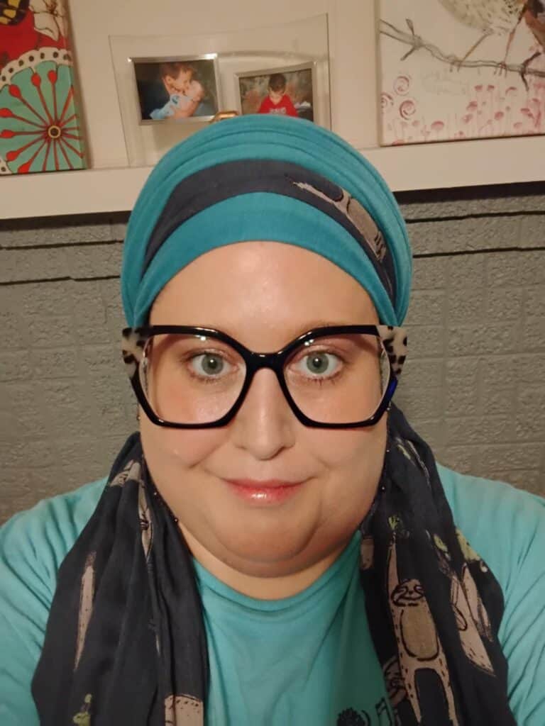Christian woman wearing a teal and navy headcovering and black cateye glasses. 