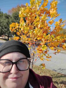 woman standing in front of a young tree with yellow leaves