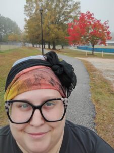 woman with headscarf in front of trees with red, yellow, and green leaves. 