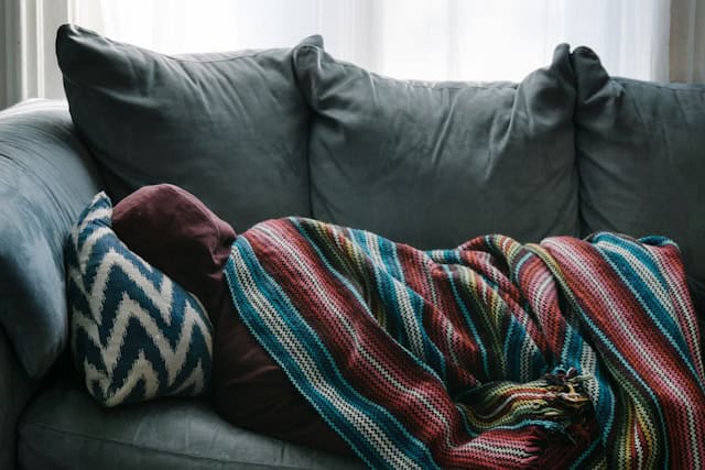 person bundled up laying a couch with back to camera