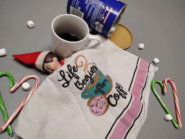 Elf on the shelf asleep surrounded by marshmallows, candy canes, and a cup of coffee